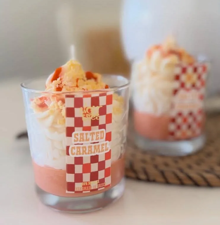 Κερί Salted Caramel: ποτήρι με ροζ κερί σόγιας και σαντιγί από κερί, με καρό ετικέτα, πάνω σε ψάθα